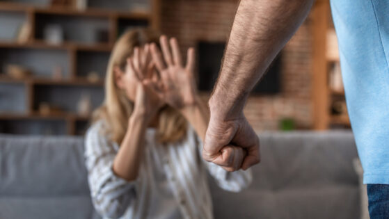 Sad crying adult caucasian wife covers her face, afraid of her aggressive husband in living room interior