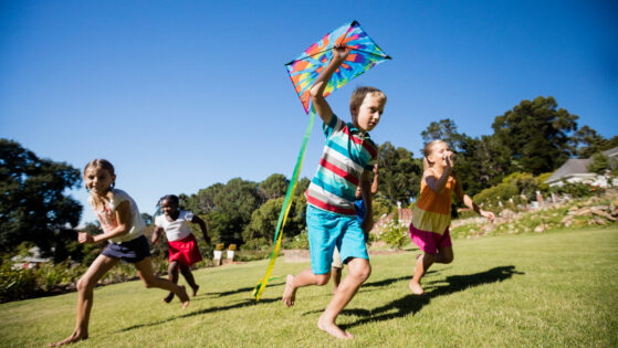 Kids playing together during a sunny day with a kite at park